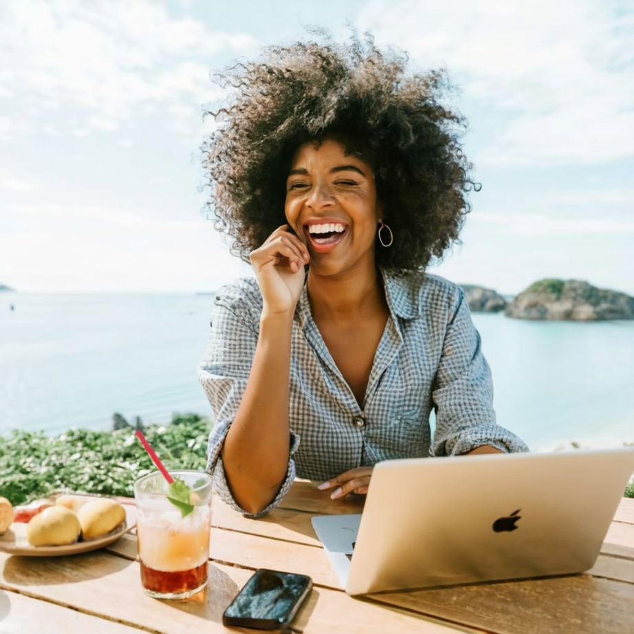 smiling person working on laptop in front of the ocean showing that she loves her life and is not settling in her work or job